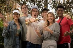 a group of young people standing next to each other in front of trees and bushes