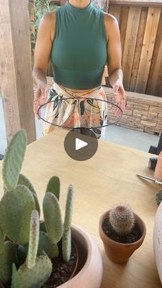 a woman standing in front of a wooden table with two cactuses on top of it