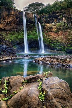 a waterfall is seen in the background with rocks and greenery on the foreground