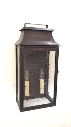 an old fashioned lantern with two candles in the middle and snow on the ground around it