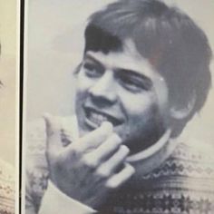 an old photo of a man smiling and holding something up to his mouth in front of him