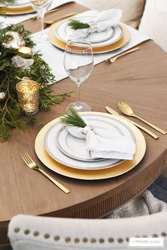 the table is set with gold and white plates, silverware, and greenery