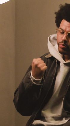 a man wearing glasses and a hoodie pointing to the side with his fist up