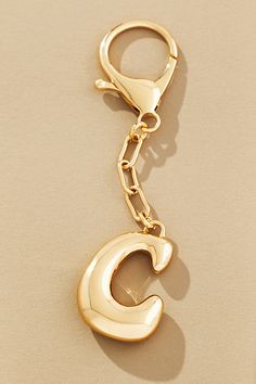 a gold key chain with the letter c hanging from it's end, on a beige surface