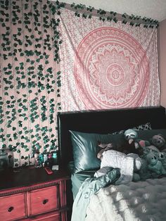 an unmade bed with pillows and stuffed animals on it in front of a tapestry