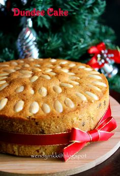 a round cake with almonds on top sitting on a wooden platter next to a christmas tree