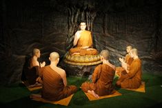 buddhas sitting on yellow mats in front of a cave like area with trees and rocks