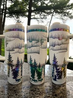 three coffee mugs sitting on top of a table next to each other with trees painted on them