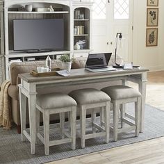 a kitchen table with four stools and a laptop on top of it in front of a tv