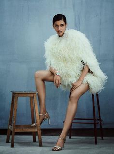 a woman sitting on top of a stool next to a wooden stool and wearing high heels