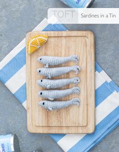 three knitted fish on a cutting board next to a can of water and an orange