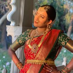 a woman in a red and green sari with gold jewelry on her head standing next to a white pillar