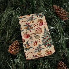 a christmas present wrapped in wrapping on top of pine branches with cones and ornaments around it