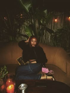 a woman sitting on top of a couch next to a table with candles and plants