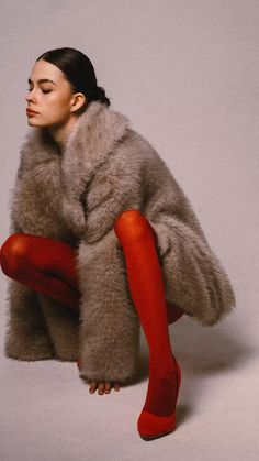 a woman sitting on the ground with her legs crossed wearing red stockings and a fur coat