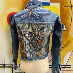 the back of a jean jacket with an eye on it, painted in bright colors