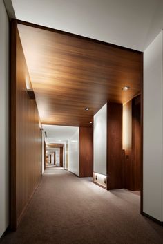 an empty hallway with wood paneling on the walls and carpeted floor, leading to another room