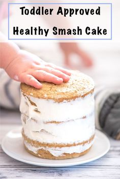 a toddler's hand on top of a healthy smash cake with white frosting