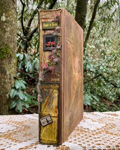 an old book sitting on top of a doily covered table in the middle of a forest