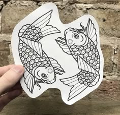 a hand holding up a sticker with two koi fish in black and white