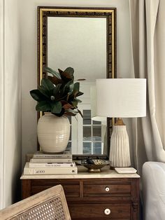 a white vase sitting on top of a dresser next to a lamp and mirror in a room