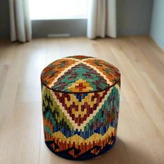 a multicolored ottoman sitting on top of a wooden floor next to a window