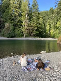 two women sitting on the shore of a lake