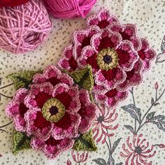 three crocheted flowers sitting on top of a table next to balls of yarn