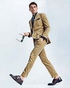 a man in a tan suit and tie walking with a pair of scissors on his feet