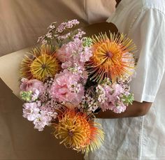 a person holding a bouquet of flowers in their hand and wearing a white shirt behind them