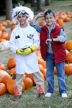 two young boys standing next to each other in front of pumpkins