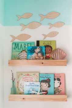 two wooden shelves with books on them and some fish painted on the wall behind them