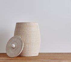 a white wicker vase sitting on top of a wooden table next to a wall