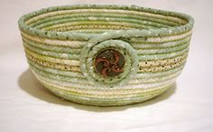 a green and white striped basket with a decorative brooch on the front, sitting on a white surface