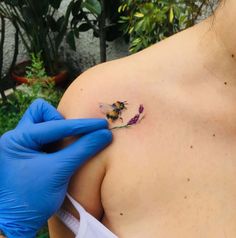 a person in blue gloves is holding up a small tattoo on their chest that has a bee on it