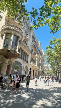 many people are walking down the street in front of some buildings with balconies