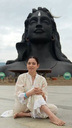 a woman sitting on the ground in front of a large buddha statue with her hands crossed