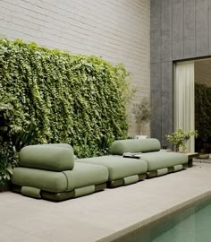 a green couch sitting next to a swimming pool in front of a wall covered with greenery