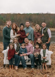 a large family poses for a photo in front of a body of water and trees