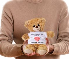 a person holding a brown teddy bear with a t - shirt that says i love you