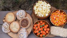 several bowls filled with different types of food on top of a wooden table next to corn, pretzels and other foods