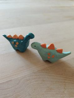 two small ceramic dinosaurs sitting on top of a wooden table, one is blue and the other is orange