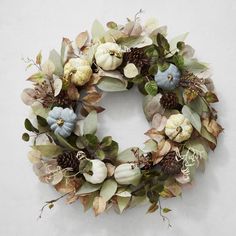 a wreath with flowers, leaves and acorns hanging on a wall in front of a white background