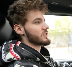 a young man with curly hair and a beard in the back seat of a car