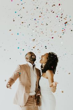 a man and woman standing under confetti falling from the sky in front of them