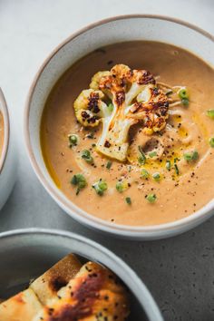 two bowls filled with soup and vegetables on top of a table next to some pita bread