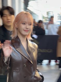 a woman in a brown leather jacket is walking down the street with her hand out