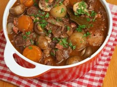 a pot filled with stew on top of a red and white checkered table cloth