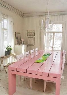 a pink table with white chairs sits in the middle of a room next to two windows