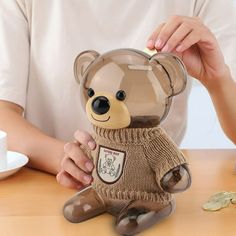 a teddy bear with a sweater on sitting at a table next to some gold coins